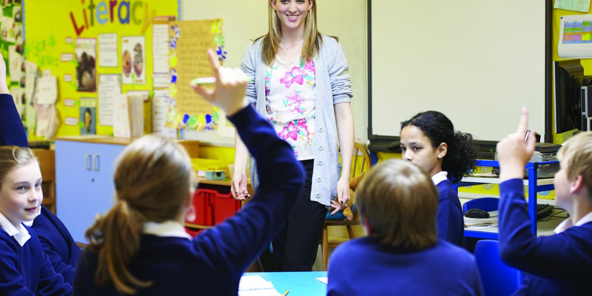 A teacher engaging students in a thoughtful classroom discussion at a whiteboard.