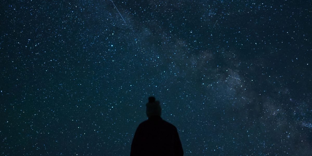 A person looks up at the vast night sky, contemplating the mysteries of the universe.
